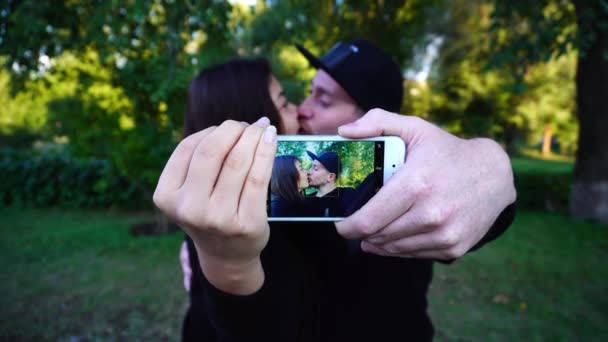 Casal amoroso segure o telefone em mãos e faça selfie, abraçando e posando para câmera no parque verde ao ar livre . — Vídeo de Stock