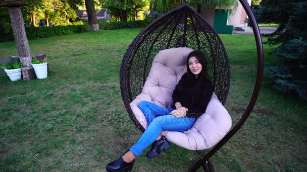 Привлекательная леди расслабляется в кресле, смотрит вокруг и улыбается, выпрямляет волосы и беседует с кем-то в парке . — стоковое видео