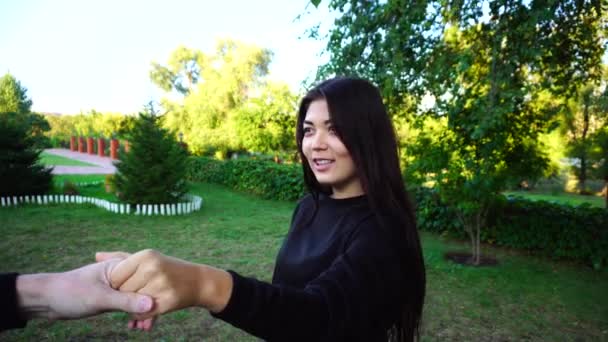 Pretty Female sostiene la mano del tipo y se comunica con su novio, sonríe y ríe, mira la cámara y posando. Chica en Green Park al aire libre . — Vídeo de stock