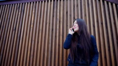 Güzel esmer kadın tutan el telefon ve konuşuyor, gülüyor ve konuşurken, gülüyor duvara açık havada duran.