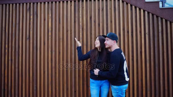 Lovers Stand in Embrace Next to Each Other and Looking Into Distance on Background Wall of Stairs Outdoors. Girl Shows Something Raising Hand Up. — Stock Video
