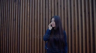 Çekici genç kadın cep telefonu üzerinde konuşurken ve ahşap duvar arka plan üzerinde gündüzleri açık havada duran.