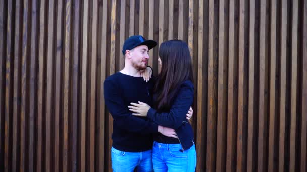 Jonge geliefden houden elkaar in sterke omarmen en kussen, ontmoetten elkaar in de buurt van houten muur van Restaurant buitenshuis in overdag. — Stockvideo