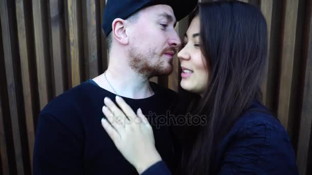 Portrait de jeune couple amoureux étreignant et embrassant devant la caméra sur fond de mur en bois à l'extérieur en journée . — Video