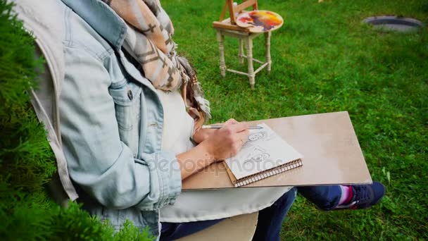 女の子アーティストの手は、無名の少女の肖像をスケッチに描いているアルバム ページに確かに鋭い鉛筆のストロークになります。公園屋外でマスターに座る. — ストック動画