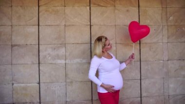 Zarif hamile sarışın gelecek arayan anne ve pozlar için fotoğraf, gülümsüyor ve taş duvar arka plan üzerinde balon yanında gündüzleri açık havada tutar.