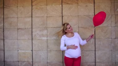Muhteşem hamile sarışın gelecek arayan anne ve pozlar için fotoğraf, gülümsüyor ve taş duvar arka plan üzerinde balon yanında gündüzleri açık havada tutar.