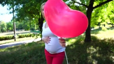 Güzel kız hamile, fotoğraf için poz ve gülümsüyor, elinde tutan ve Park havada duran Ballon, karın, okşayarak bakar.
