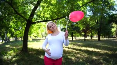 Muhteşem hamile genç bayan poz için kamera ve gülümsüyor, Asansör yukarı ve parkta gündüz açık havada duran Ballon, şefkatle dokunmadan göbek, bakar.