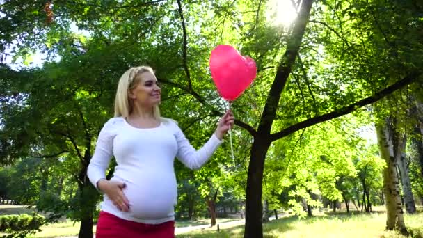 Mujer encantadora para esperar, posando para la cámara y sonrisas, levantar y mira el balón, acariciar la barriga, de pie en el parque durante el día al aire libre . — Vídeos de Stock