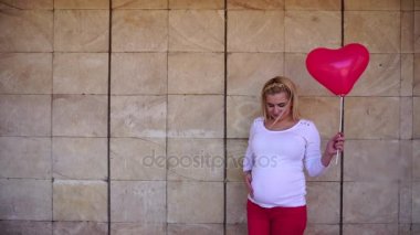 Çekici genç kadın balon elinde tutan bebek bekliyor ve kamerayı, bakar gösterir jest, taş duvar açık arka plan üzerinde duruyor.
