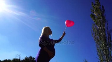 Harika Bayan olması bekleniyor Holding ve Ballon arka plan mavi gökyüzü, pozlar ve okşayarak karnında Park açık havada elinde bakar.