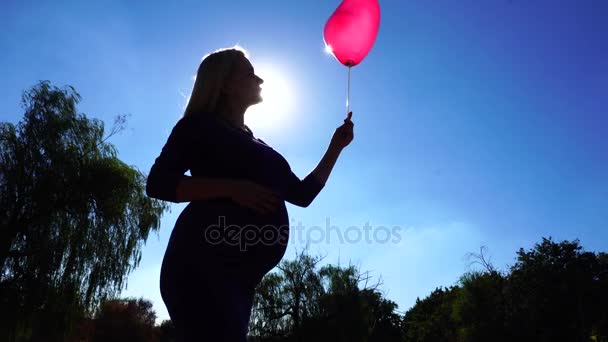 精彩的小姐要期待着和看着气球在手，纠正在蓝色天空背景和抚摸肚子在公园户外的头发. — 图库视频影像