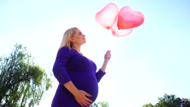 Magnifica futura madre che tiene e gira palloncini in mano sullo sfondo della luce del sole, posa e sorride dolcemente, accarezzando la pancia . — Video Stock