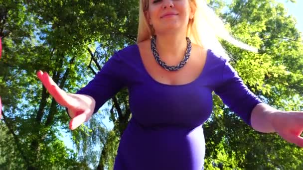 Потрясающая беременная девушка расправляет шары по сторонам улыбаясь и позируя прямо в камеру, стоя в зеленом парке на открытом воздухе днем . — стоковое видео