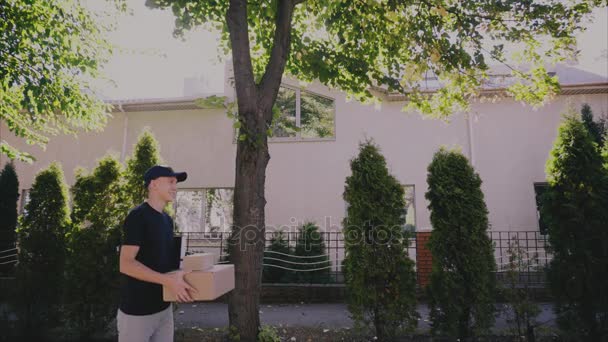 Junger Mann Kurier trägt Paket in den Händen, lächelt in Kamera auf Hintergrund von Bäumen, Person beschäftigt, um Waren zu liefern . — Stockvideo