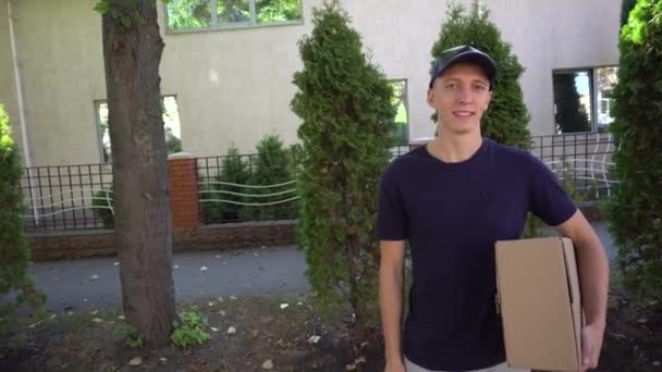 Corriere pedonale Grande ordine in mano e sorridente alla macchina fotografica sullo sfondo di alberi e casa, stand all'aperto durante il giorno . — Video Stock