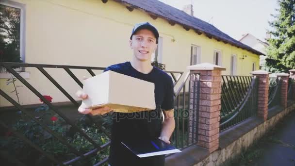 Muž Courier přináší se usmívá na kameru na pozadí stromů, aby osoba, která zboží doručeno. — Stock video