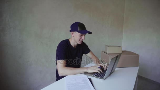 男はテーブルの前に座って、仕事にコンピューターは、郵便局に仕事で必要な情報を記録. — ストック動画