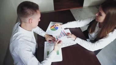 Adam ve kadın iş hakkında söyler grafik gösterir. Onlar ahşap masa ve sıkışalım ofisinde oturan.