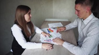 Kadın adam iş, yeni fikirleri tartışmak ve grafik gösterir. Onlar oturan ofis ahşap masaları ve adam gibi değil o sinir ve kağıt kaldırır.