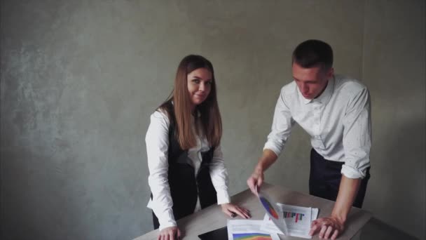 Хлопчик і дівчинка стоять біля столу і хлопець емоційно показує на папері з діаграмами в робочому офісі . — стокове відео