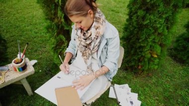 Ressam kadın yapma konturlar ve kurşun kağıt ve grafik kalem ve tutar el kullanma. Gündüz vakti Park açık havada kız oturuyor.