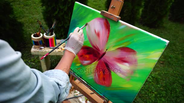 Hand van vrouwen kunstenaar leidt borstel op groene achtergrond op Canvas en gemengde kleuren tegen de achtergrond van groen gras en Bench met Art Tools Outdoors. — Stockvideo