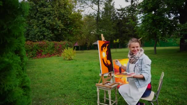 La deslumbrante artista femenina admira el cuadro y dibuja los últimos detalles y obras en el parque sobre el fondo de las plantaciones verdes de Cool Autumn Day al aire libre . — Vídeos de Stock