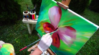 Güzel sanatçı tutar fırçalar ve yazar resim ve arka plan yeşil çim ve sanat ile tezgah üzerinde Park tribünlerde araçları açık havada.