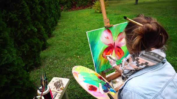 Chica artista dibuja cuadro y sentado con la espalda a la cámara en la silla en el parque al aire libre en otoño . — Vídeos de Stock