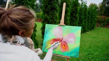 Sanatçı kadın özetliyor kelebek kanatları başlayan ve iğne yapraklı ağaçlar açık havada arka plan üzerinde kamera Park için geri şövale oturan.