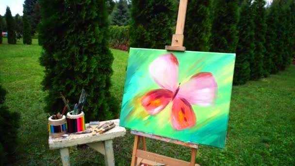 Peintures à l'huile complétées et détails des articles artistiques qui se tiennent sur le chevalet et la table dans le parc à l'extérieur . — Video