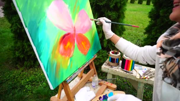 Olśniewające szczotki posiada osoba płci żeńskiej twórczy i zapisuje obraz w parku na tle zielonych plantacji na zewnątrz w dzień wiosny Cool. — Wideo stockowe