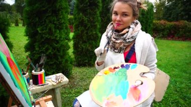 Portre ressam poz, hoş bir fotoğraf makinesi ile fırçalar ve paleti içine gülümseyerek parkta gündüzleri açık oturur.