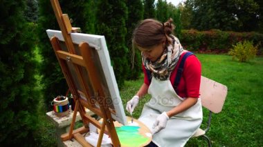 Kadın sanatçı fırça boya ve Mix renk paletinde, tezgah sanat ile yakın oturur kazanıyor araçları açık havada.