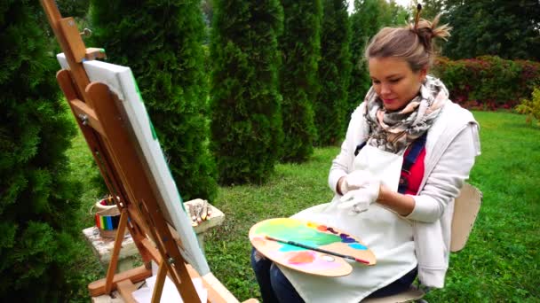 Ženy jemné malíř dát rukavice na rukou, s úsměvem do kamery a sedí v parku venkovní. — Stock video