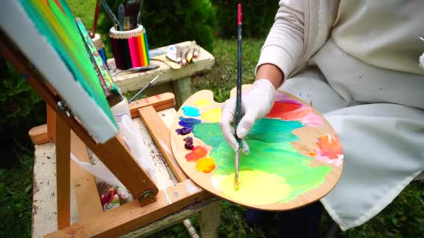 欧洲外观艺术家认为调色板和画笔，女混合黄色颜色与在画布上的另一种颜色，使第一笔画公园户外. — 图库视频影像