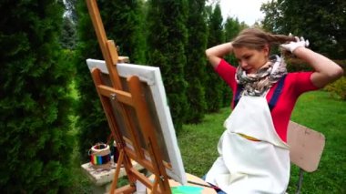 Fırçalar ve palet, saç at kuyruğu ve kameraya poz ipe çizim önce güzel ressam boyalı kadınlar ayakta Park'ta açık.