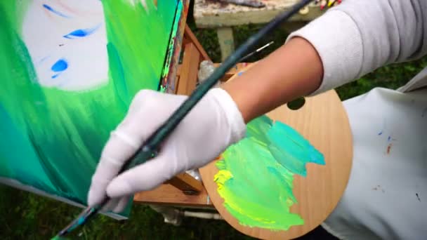 Belle artiste tient pinceaux et écrit photo et assis dans le parc sur fond d'herbe verte et banc avec des outils d'art en plein air . — Video