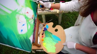 Liseli kız Sanat Okulu fırça elinde tutan boya renkleri arka plan ve tuval üzerinde palet tutar bacaklar ve oturur Park açık havada kurşun.