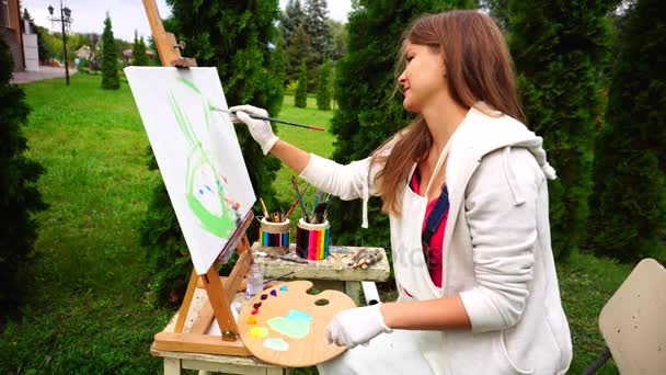 Mulheres elegante pintor marca contornos de futuras asas de borboleta, pintado com pincéis e paleta, senta-se no parque durante o dia . — Vídeo de Stock