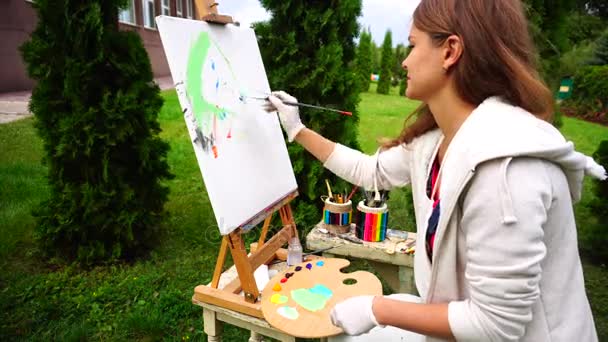 Стильный художник держит кисти и рисует быстрый эскиз будущей картины в парке на фоне деревьев под открытым небом . — стоковое видео