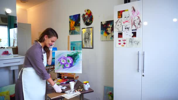 Artist Girl Picks up Phone in Order to Answers Call, Stands in Art Studio on Background of Wall With Pictures. — Stock Video