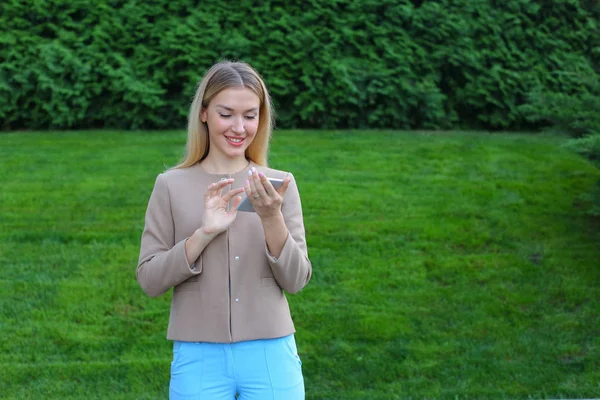 Hermosa mujer mirando la pantalla del teléfono inteligente y sonríe, se para — Foto de Stock