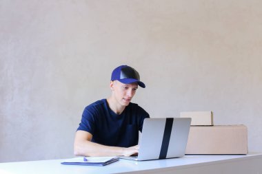 Postane bilgisayarda yazarak masada oturan kurye.