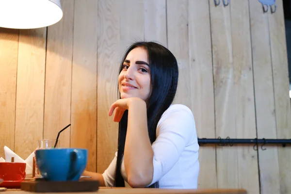 Chica bonita sonriendo, posando y mirando en cámara en la mesa en co — Foto de Stock