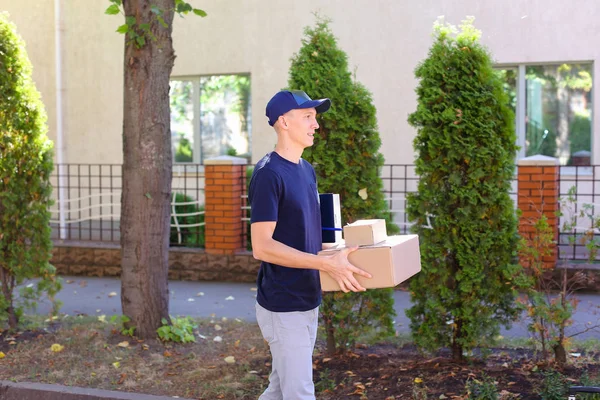 Joven mensajero llevando la orden en las manos, sonriendo a la cámara y — Foto de Stock