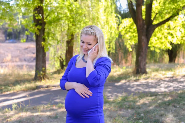 Elegancka Kobieta w ciąży idzie i mówić na gadżet na drodze wzdłuż — Zdjęcie stockowe