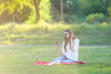 gülümseyen ve onun laptop müzik çalışma parkta oturan genç kız